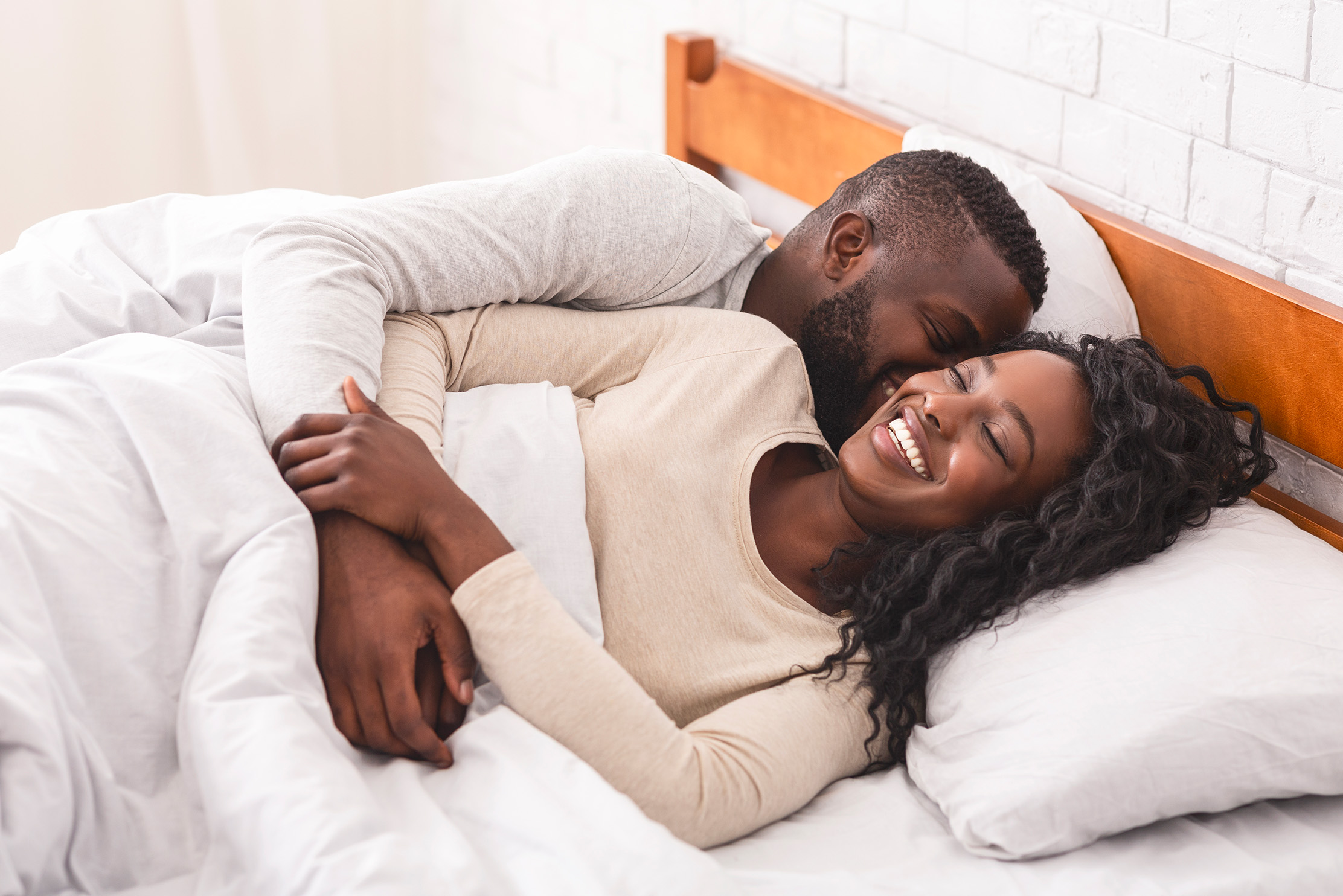 A black couple cuddle and laugh in bed