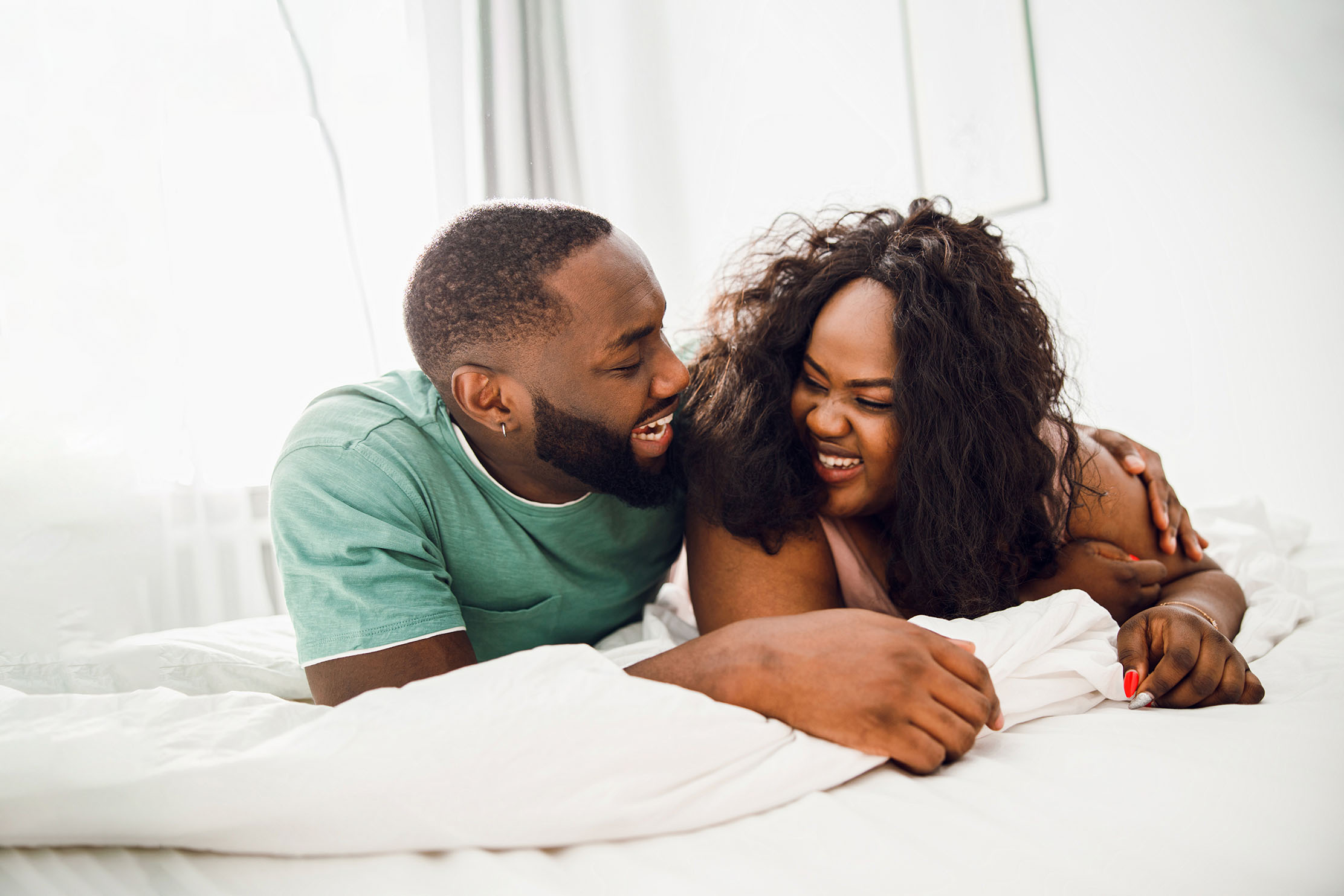 A black couple laugh in bed together